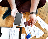 Person Holding Phone and Credit Card with Various Bills on the Floor